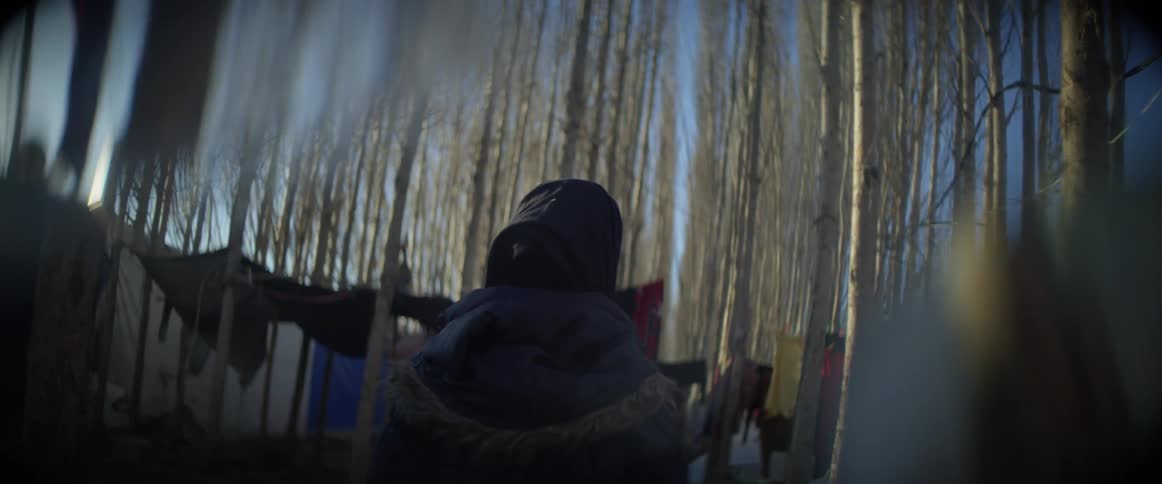 A person is wearing a coat as they walk through a refugee camp in daylight