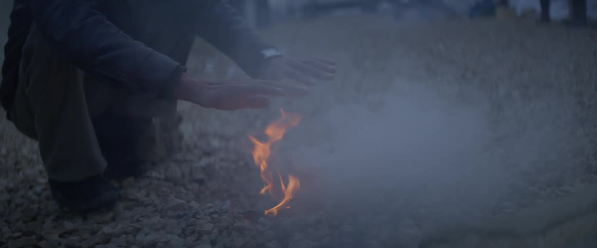 A person warms their hands over a fire burning outside