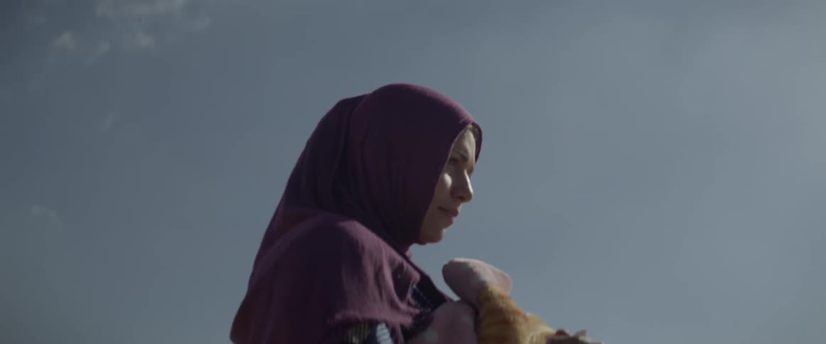 The woman is carrying some blankets on a sunny day