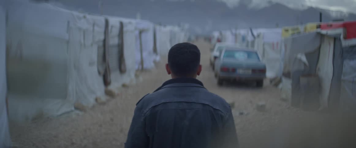 Man walks by a row of white tents in the evening