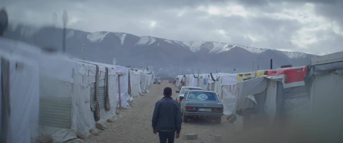A man is walking through a refugee camp on a winter day