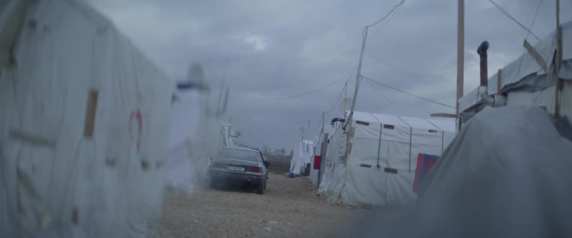A car is parked on the dirt road in a tent city on a cloudy day