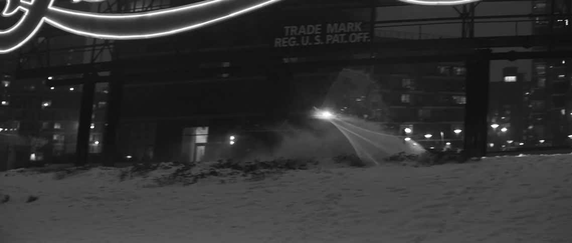 A truck plows snow on a city street at night