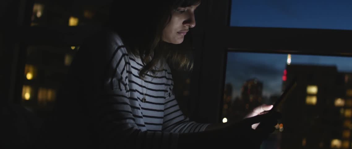 Woman using a tablet near a window at night