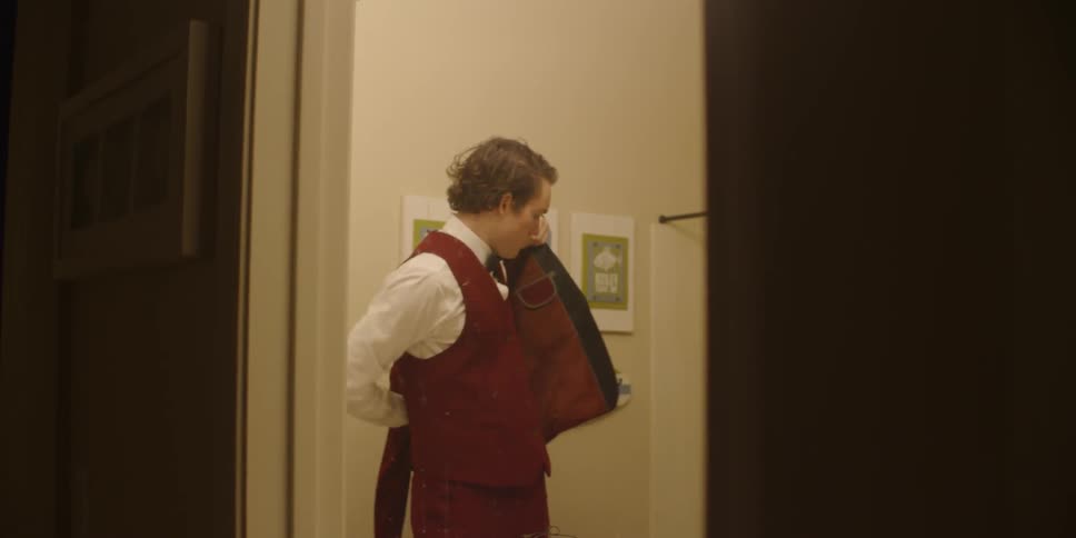 A teenage boy is putting on a tuxedo inside a bathroom at night