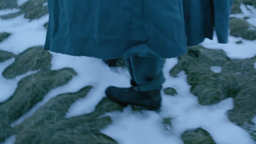Man in a long coat walks through the snowy field