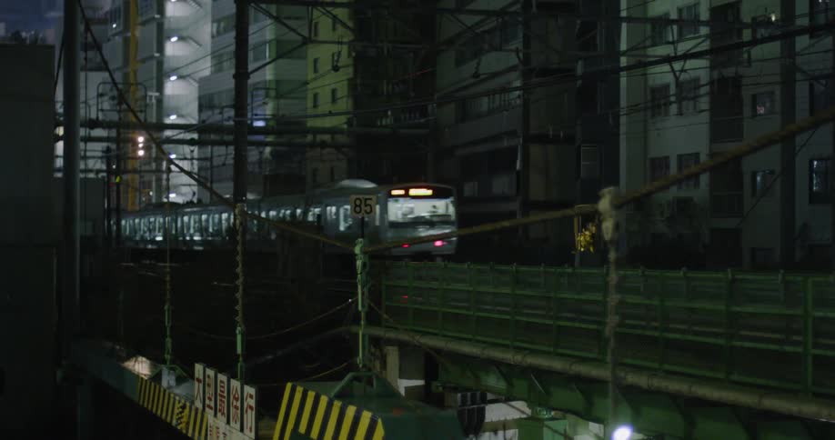 Train passes by tall buildings in a city at night