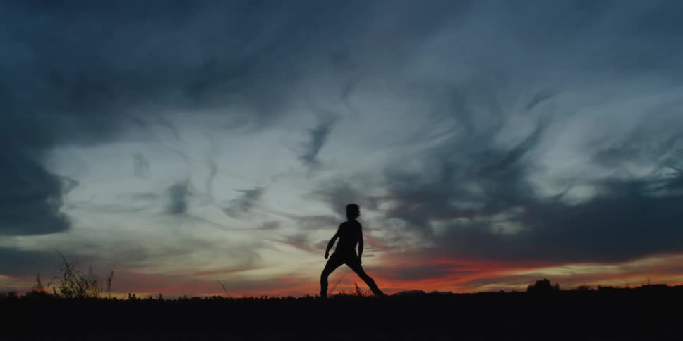 Man dances beneath the sky at sunset