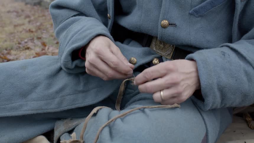 A soldier sits on the ground and sews two straps together