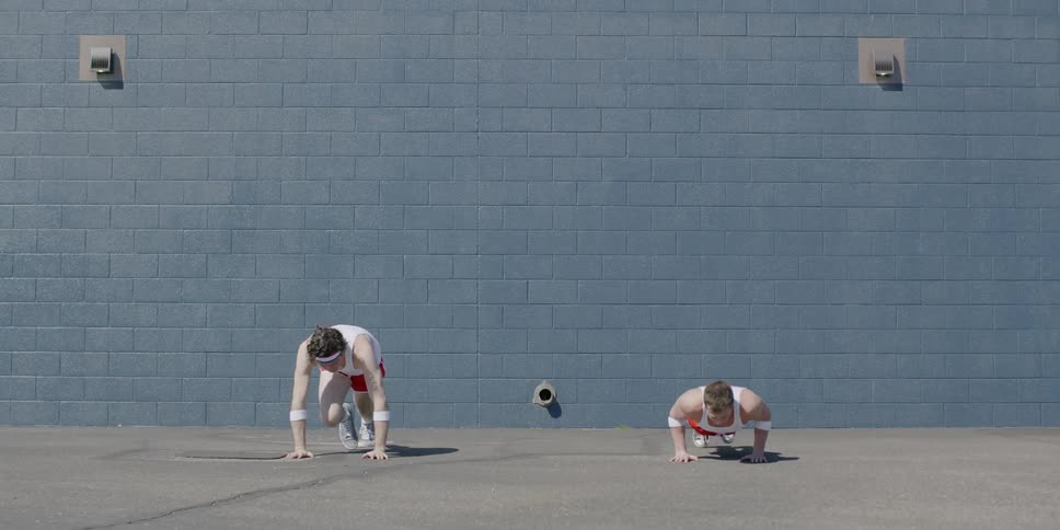 Two men exercise together by a concrete wall