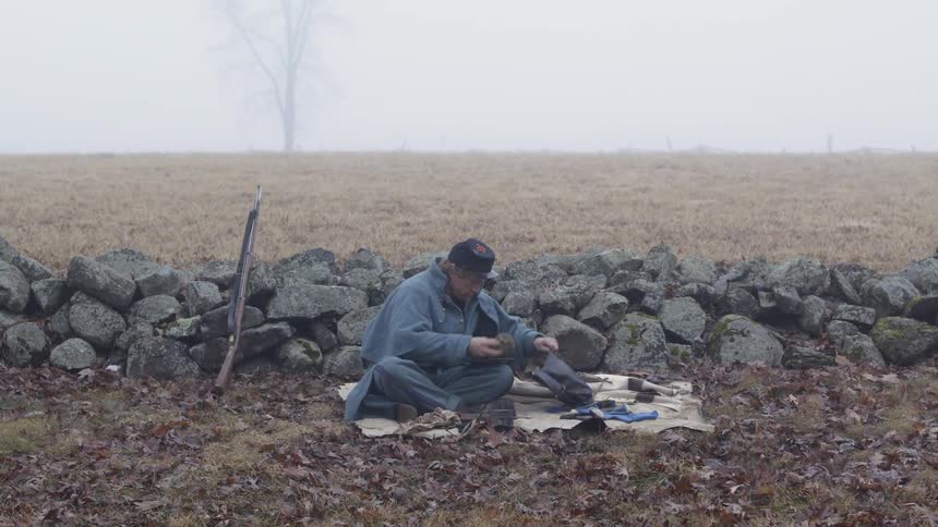 Civil war reenactor sits by stone wall and organizes his kit