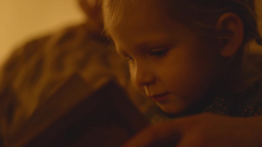 A girl looks at a book as her mom turns the pages
