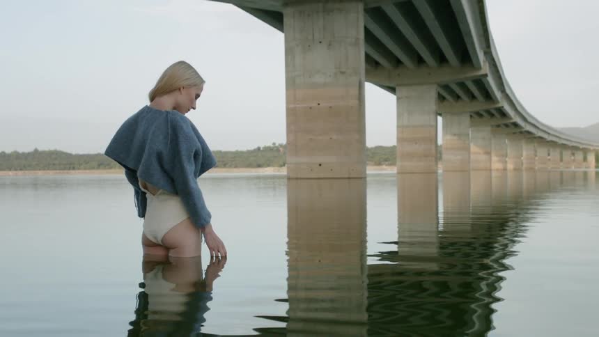 A woman is standing in the shallow water under the bridge
