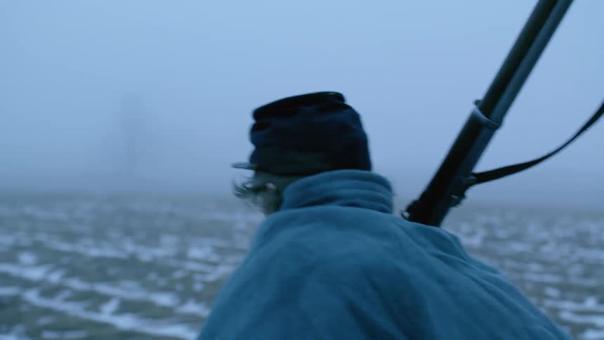 Soldier walks outside in a snowy field carrying a gun