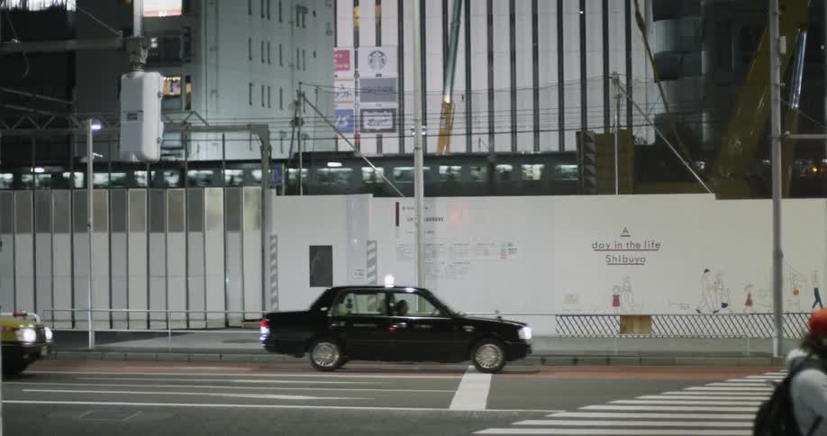 Several vehicles drive in a city with a train passing overhead on a bridge