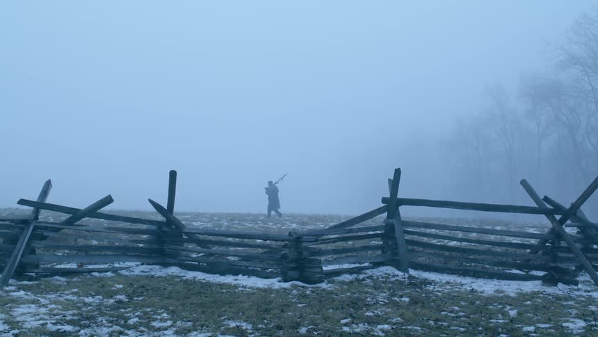 Person walks in a snowy field and a rickety broken fence