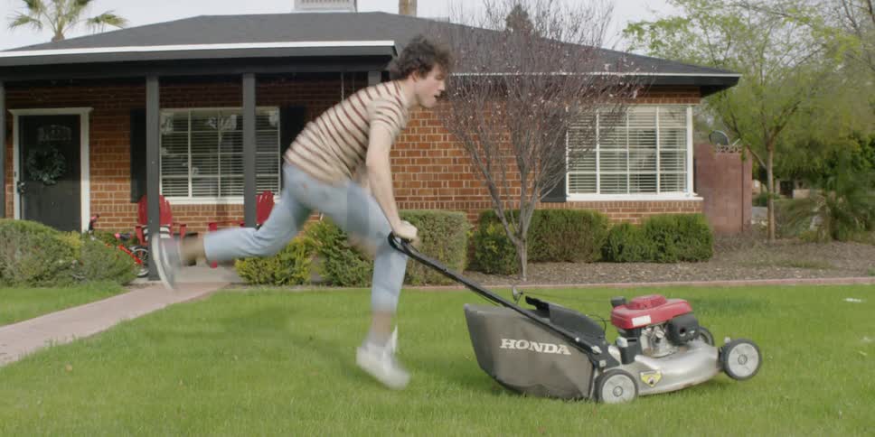 A young man dances while mowing the lawn