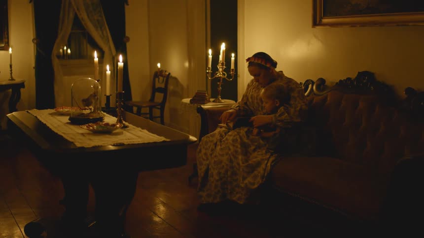 Woman sits with a child in a dim room lit with candles