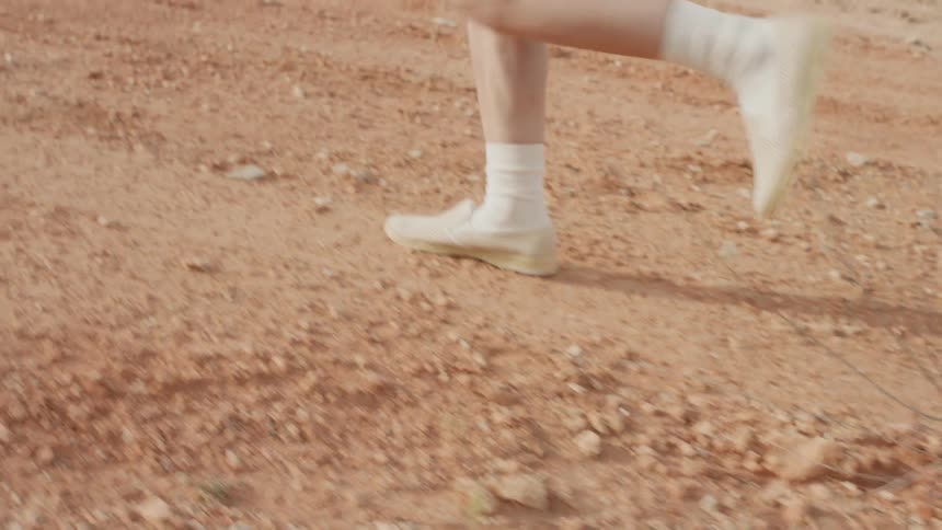 Man wearing white socks and shoes runs over the sand