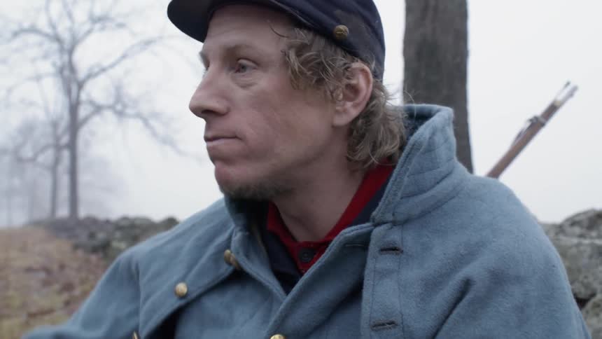 Man wearing a hat eats a sandwich and wipes his mouth on his sleeve