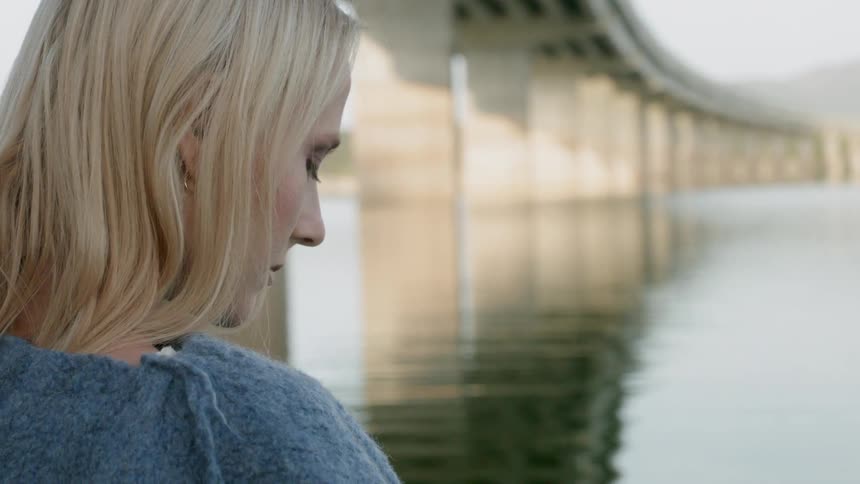 A woman looks down at the water under a bridge