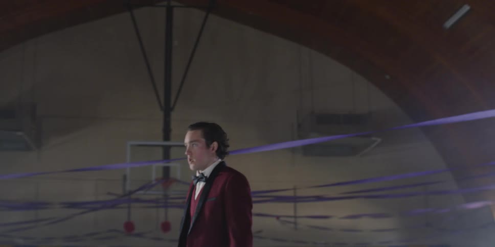 Man wearing a suit stands in the middle of a gym with balloons on the floor