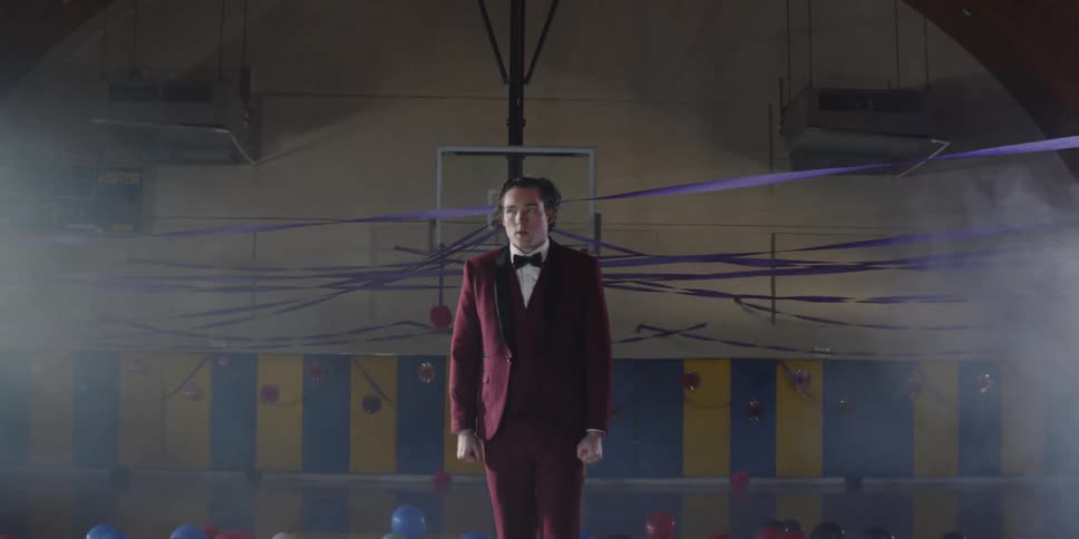 Scared looking teenager wearing a suit stands in the gym near balloons