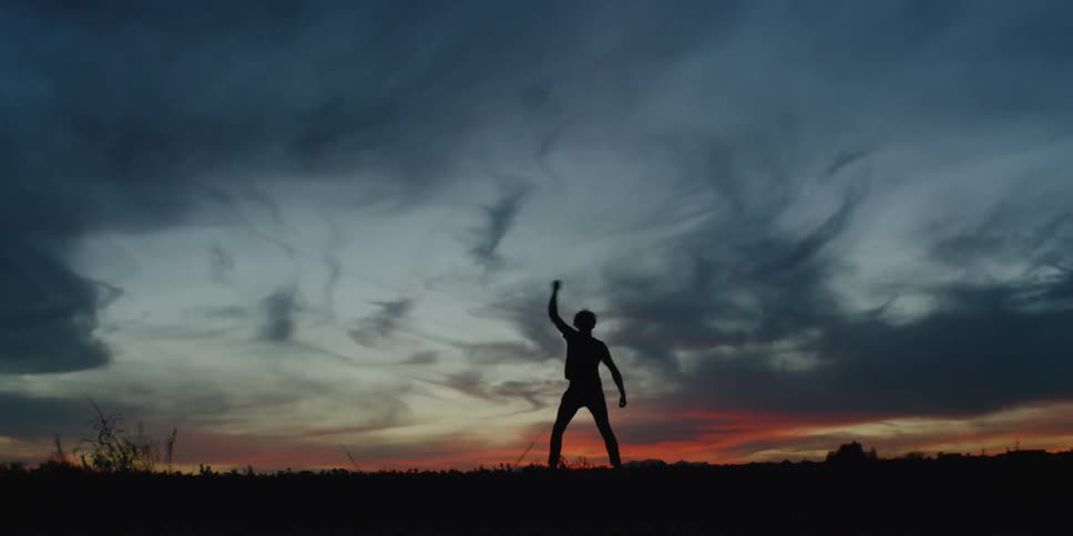 The silhouette of a man dancing on the side of the road at sunset