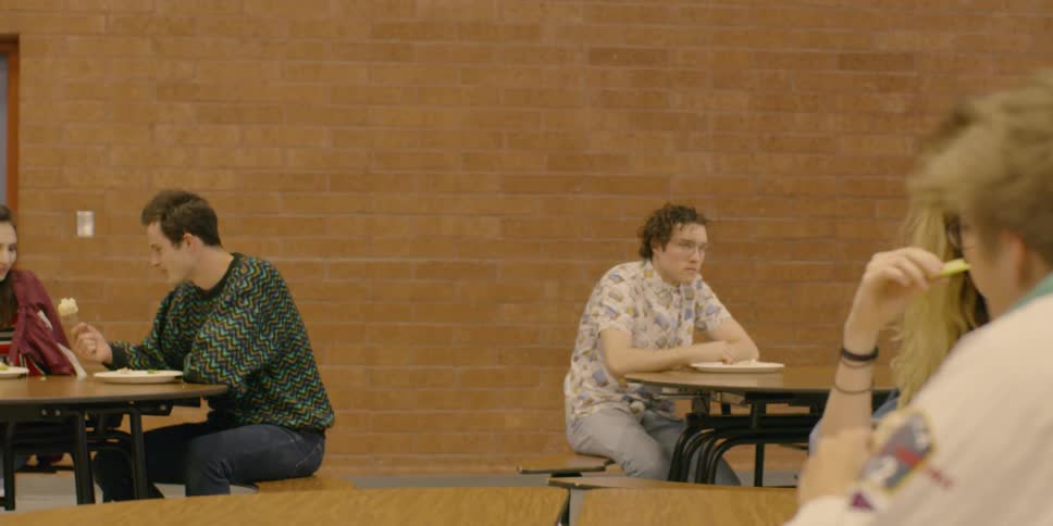 Two teenagers sit in a cafeteria eating