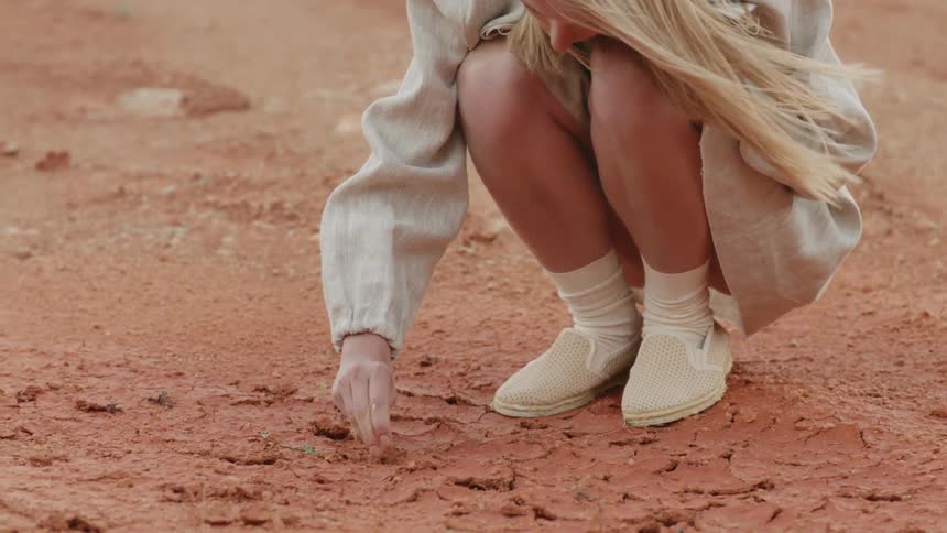Blonde woman crouches as she touches the sand
