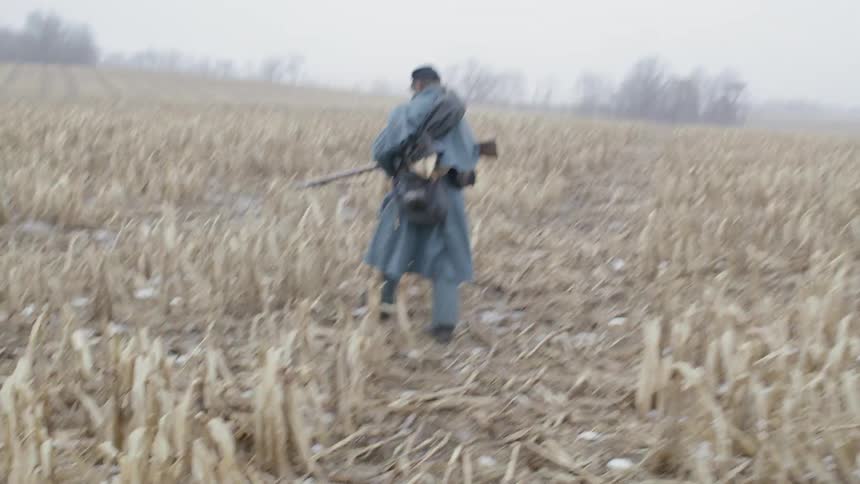 A soldier walks through a field with a rifle