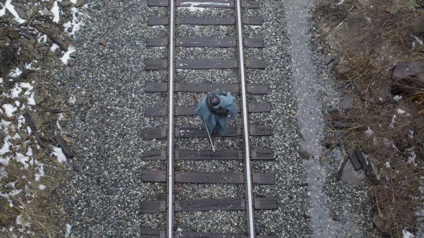 Man carrying a gun walks down train track