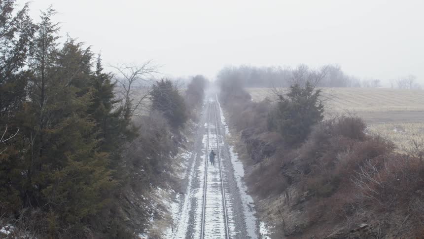 Person walks down snowy railroad tracks