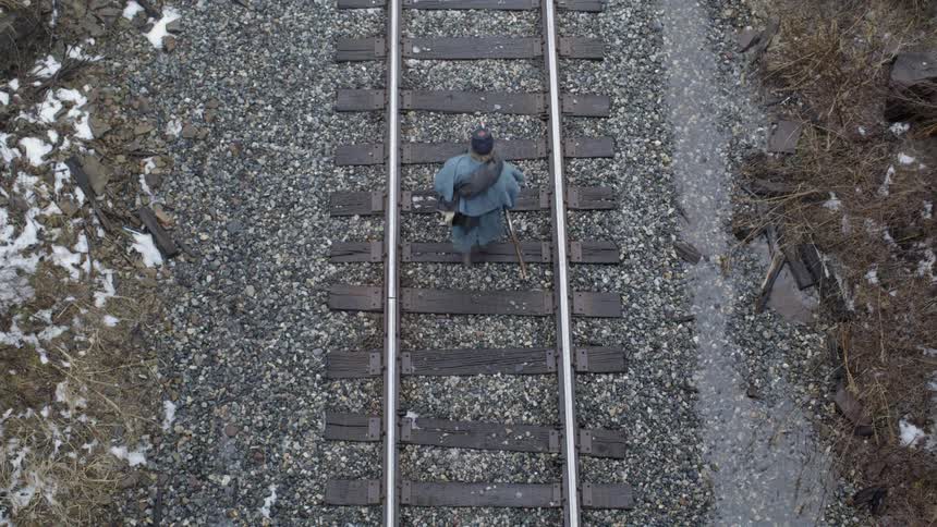 A soldier is carrying a rifle as he walks on train tracks in winter