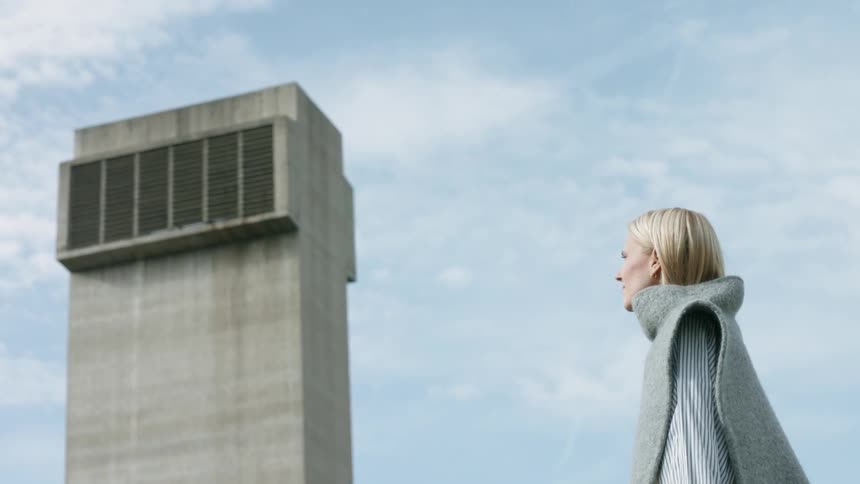 A woman stands outside near a building tower on a sunny day