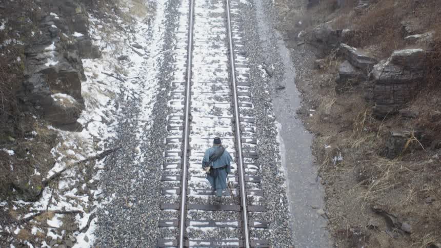 Man carries a rifle as he walks down the train tracks