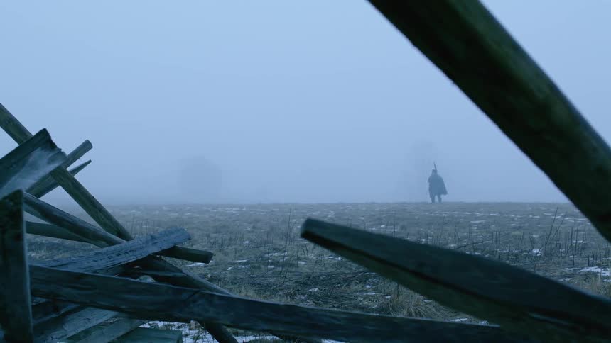 Past the planks of wood a man is hiking on the field