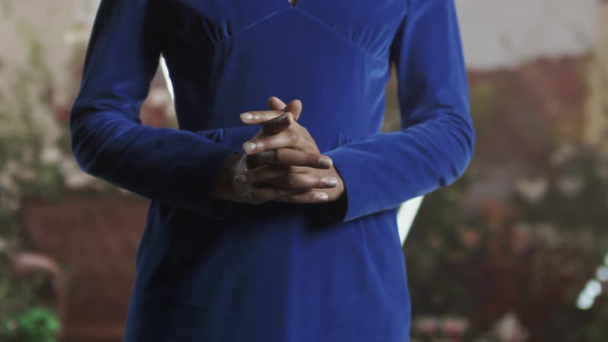 A woman wearing a blue dress is clasping her hands together