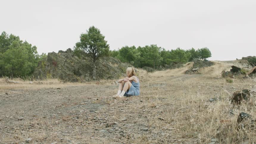 A woman sits in the dirt on the hill
