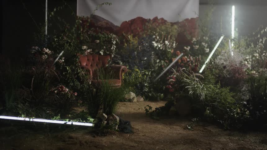Fluorescent lights are flashing as they stand arranged on a set with flowers and dirt