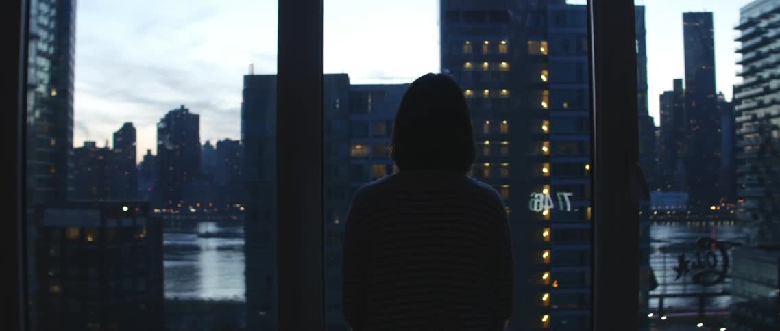 A person looks through floor-to-ceiling windows at a city