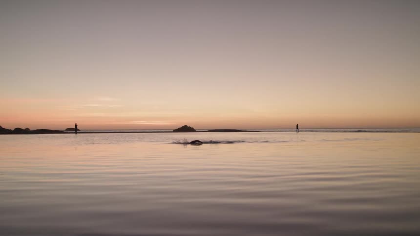 A person is swimming in a lagoon at a beach at sunset