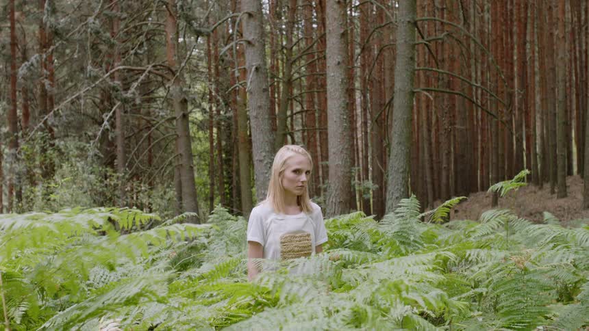 Woman stands in tall bushes in the forest
