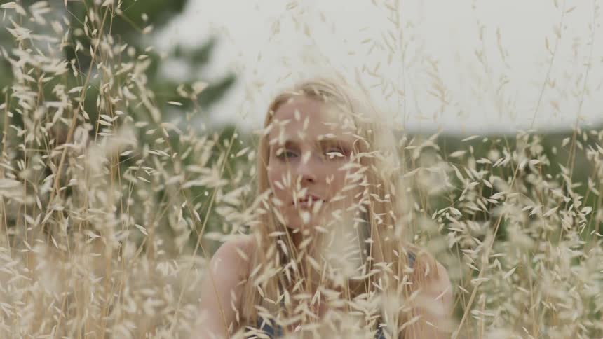 Woman sits in a weedy field on a cloudy day