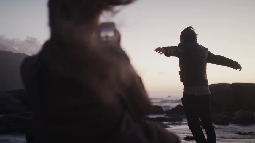 A woman photographs a man leaning into the heavy winds