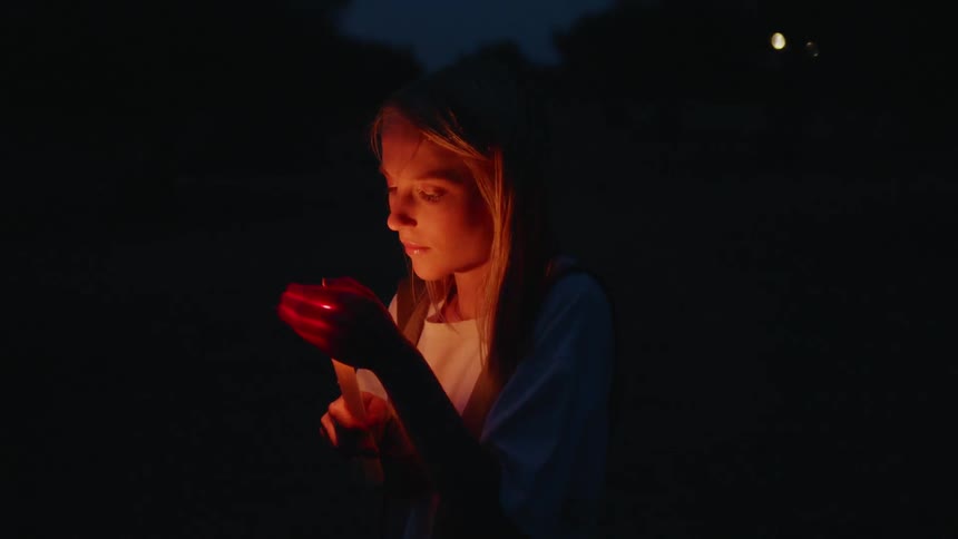 A woman holding a candle outside protects the flame with her hand