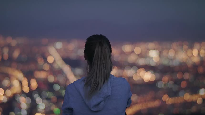 A blond haired woman stands atop a hill overlooking the city