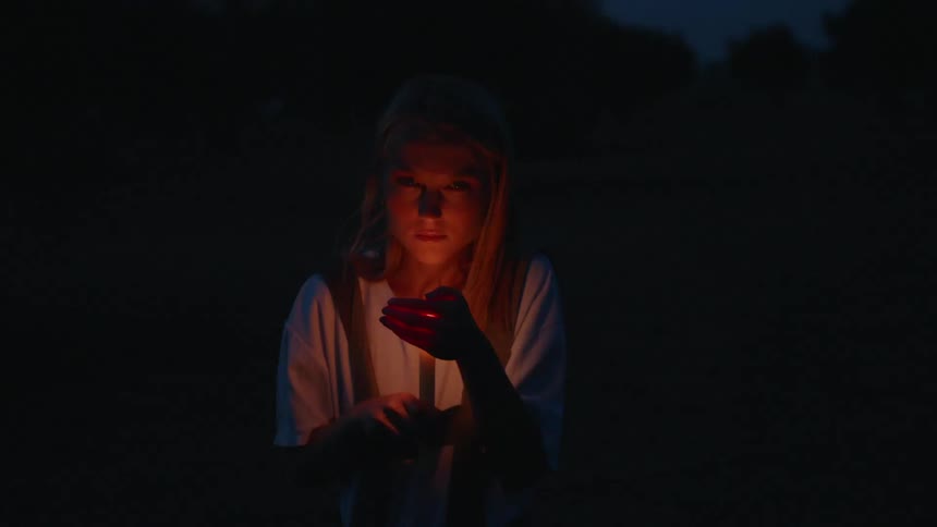 A woman sits in the dark as a candle flickers in front of her face
