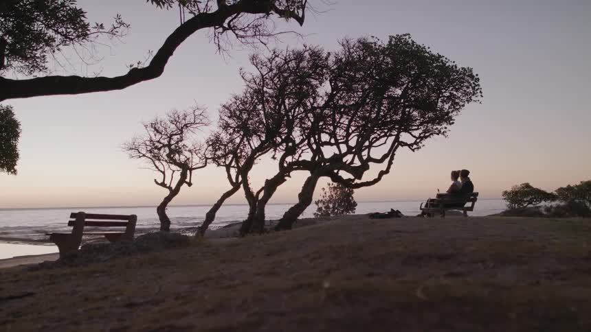 Two people are sitting on bench by lake after sunset