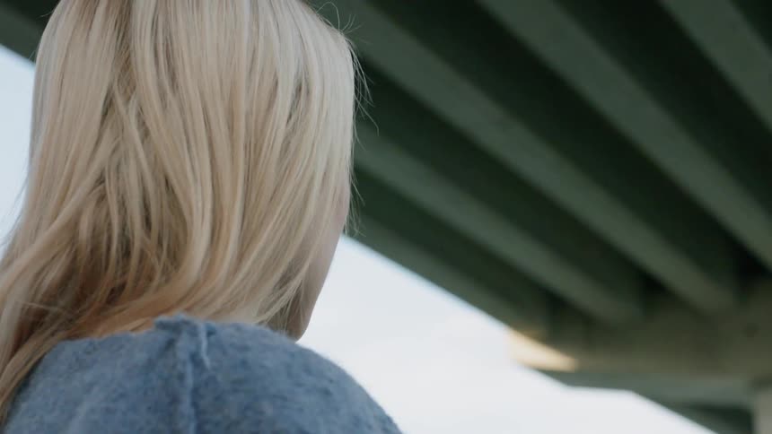 A woman stands under the bridge on a windy day